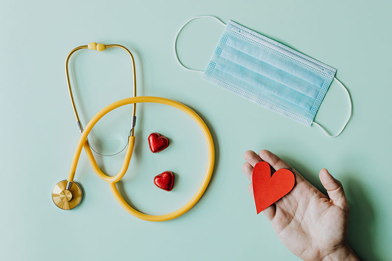 Una mano sosteniendo un corazón un cubre bocas y un estetoscopio. Una mano sosteniendo un corazón un cubre bocas y un estetoscopio.