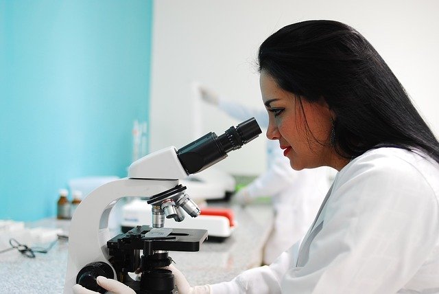 Mujer con bata blanca en un laboratorio haciendo uso de un microscopio