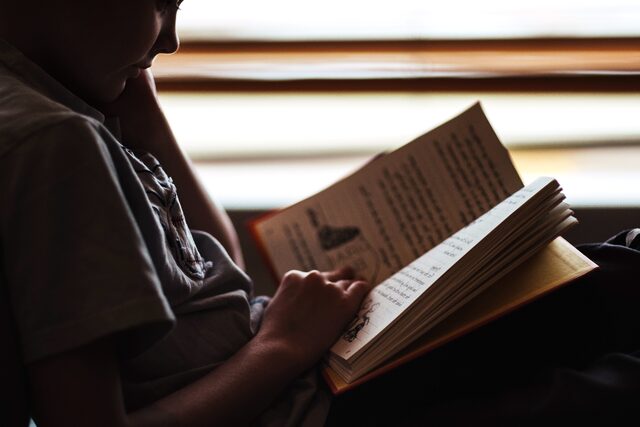 niño sentado que sostiene y lee un libro