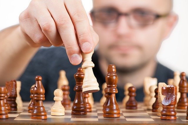 tablero de ajedrez con sus piezas y una mano tocando una de ellas