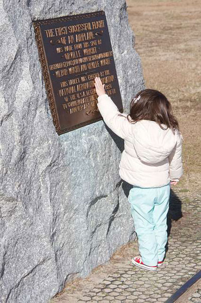niña tocando el texto de una placa histórica