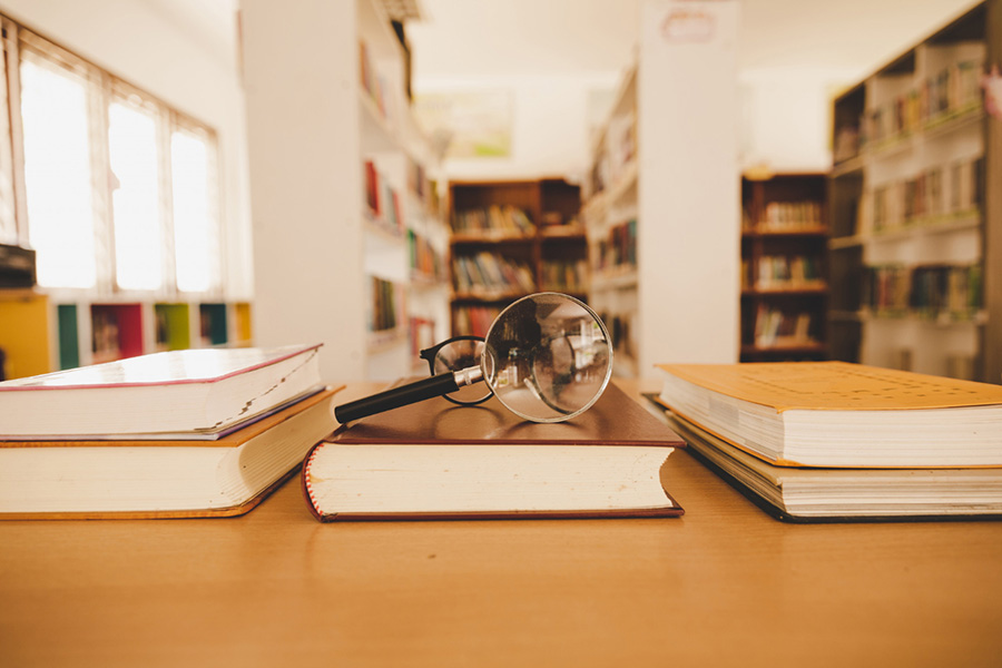 Lupa sobre libro dentro de una biblioteca.