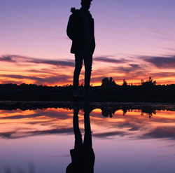 Una persona reflexionando y su reflejo en el agua