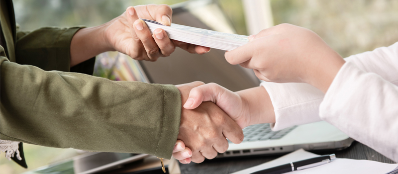 Dos hombres de negocios dándose la mano e intercambiando dinero.