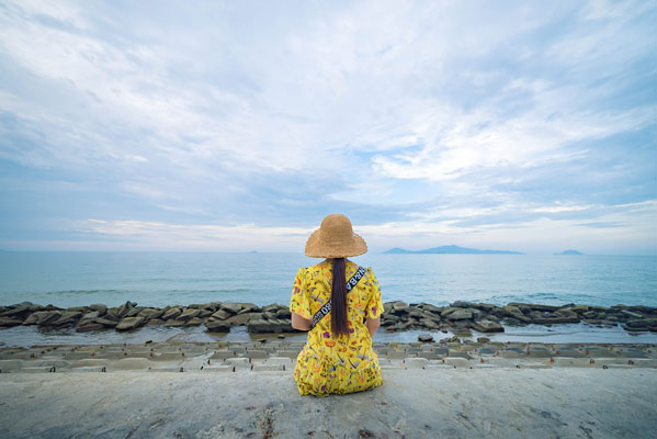 mujer vista de espaldas con sombrero y vestido amarillo contempla el mar