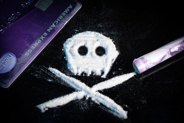 una calavera formada con polvo blanco (que hace alusión a la cocaína), una tarjeta de crédito y un billete hecho rollito.