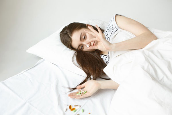 mujer joven vestida con ropa de calle en la cama sosteniendo varias pastillas en la mano