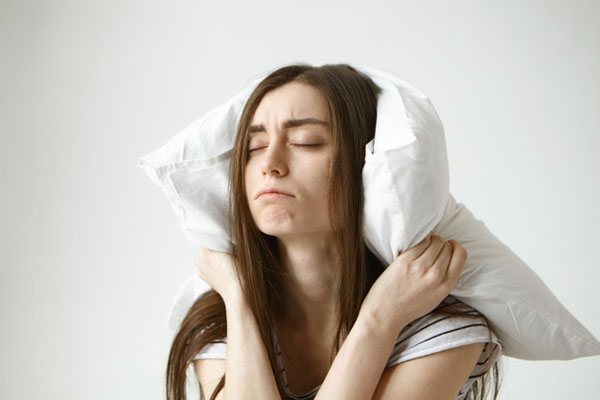 mujer con los ojos cerrados jalando una almohada sobre su cabeza