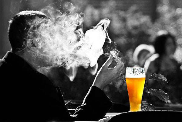 silueta de un hombre sentado en la barra de un bar con una nube de humo de cigarro y un vaso grande de cerveza.