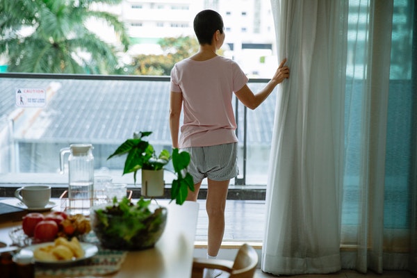 mujer viendo por una ventana, se ve un plato de comida saludable y plantas