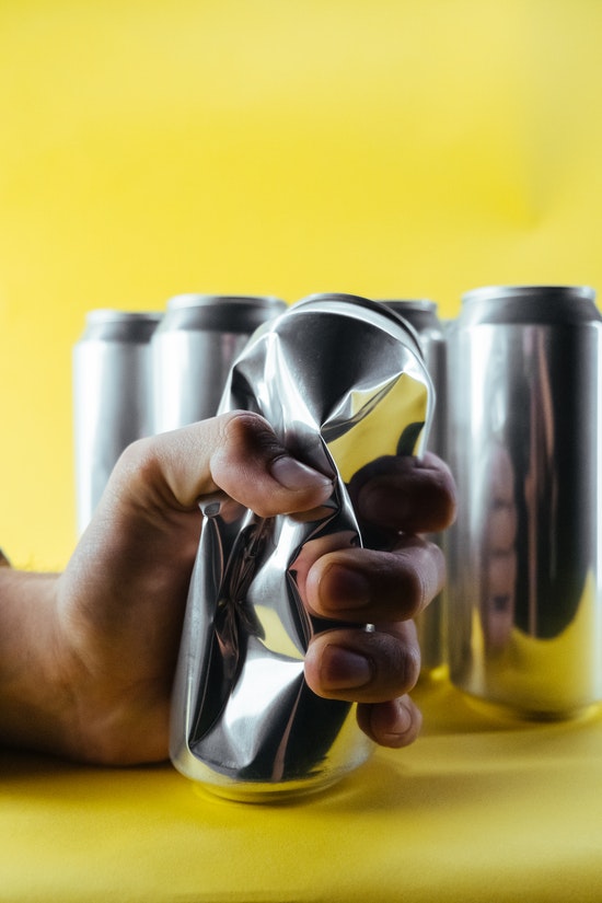mano que aplasta una lata de cerveza en fondo amarillo
