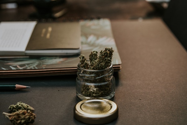 pote de vidrio con marihuana sobre un escritorio con cuadernos y un lápiz