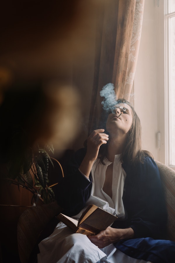 mujer fumando un cigarro de marihuana mientras lee
